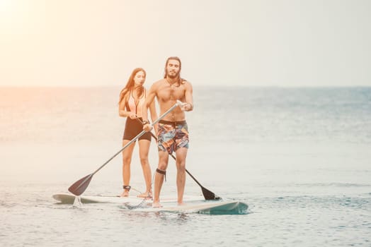 Sea woman and man on sup. Silhouette of happy young woman and man, surfing on SUP board, confident paddling through water surface. Idyllic sunset. Active lifestyle at sea or river