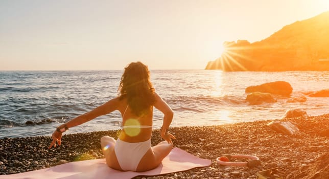 Young woman in swimsuit with long hair practicing stretching outdoors on yoga mat by the sea on a sunny day. Women's yoga fitness pilates routine. Healthy lifestyle, harmony and meditation concept.