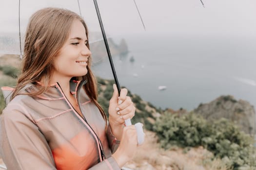 Woman rain park. Happy woman portrait wearing a raincoat with transparent umbrella outdoors on rainy day in park near sea. Girl on the nature on rainy overcast day