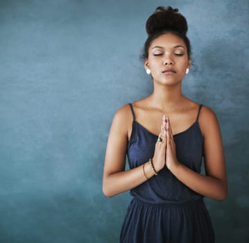 Cropped shot of a young woman meditating against a grey background.