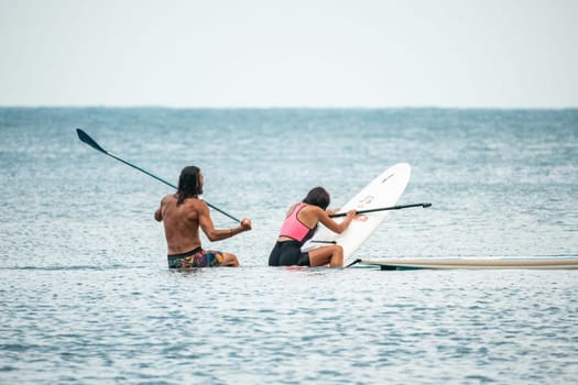 Sea woman and man on sup. Silhouette of happy young woman and man, surfing on SUP board, confident paddling through water surface. Idyllic sunset. Active lifestyle at sea or river