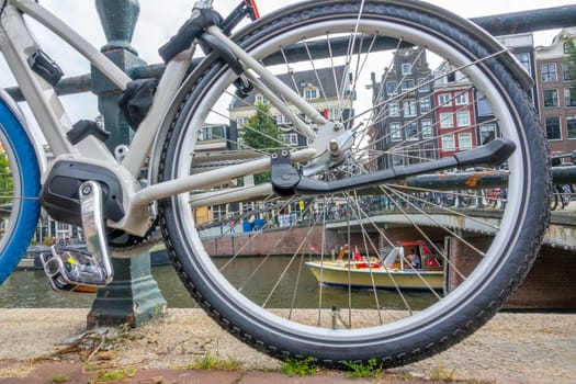 Netherlands. Summer day on the Amsterdam canal. Big bicycle wheel and authentic quay buildings