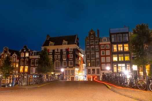 Netherlands. Summer night in Amsterdam. Bicycles are parked at the fence of the bridge over the canal and typical Dutch buildings on the quay