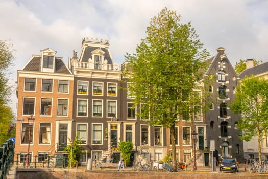 Netherlands. Facades of typical buildings on a summer street in Amsterdam. People, bicycles and cars on the canal quay