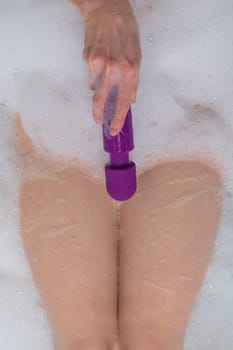 A woman lies in a bubble bath and holds a purple vibrator