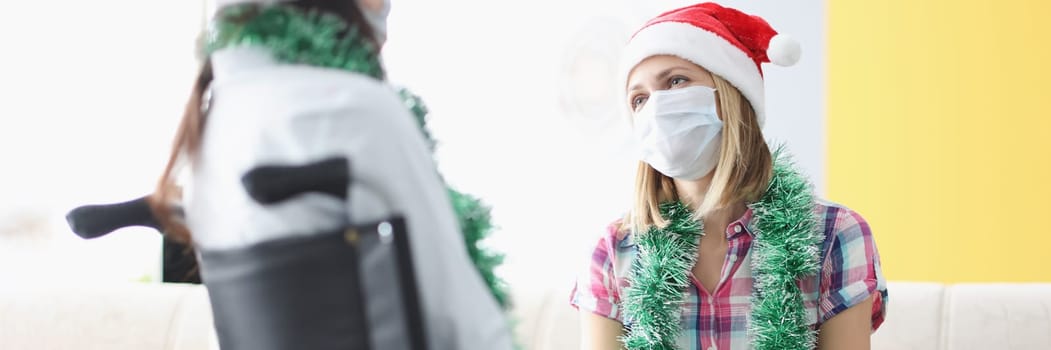 Portrait of female visiting sister in clinic, relative sitting in wheelchair, face mask for protection. Healthcare, medicine, disabled people, family, pandemic, new year concept