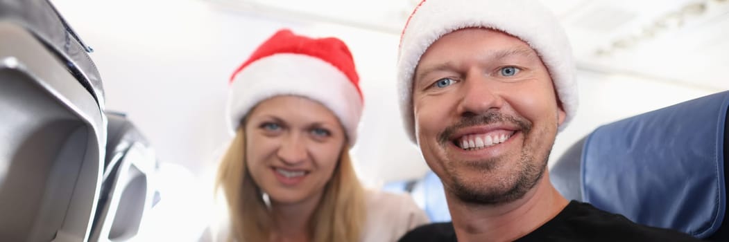 Man and woman in red santa hats flying in airplane. New years and christmas celebrations abroad concept