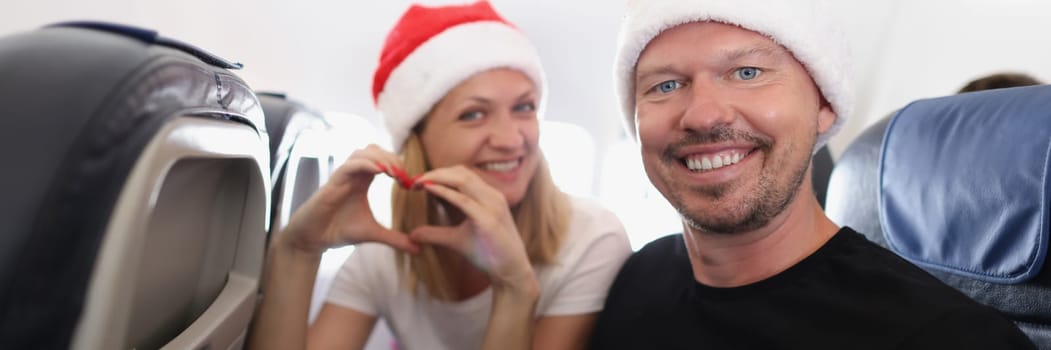 Portrait of joyful couple send love to people, man show thumbsup, wishing happy new year, woman and man wear festive hats. Celebrate new year on airplane, christmas, flight concept