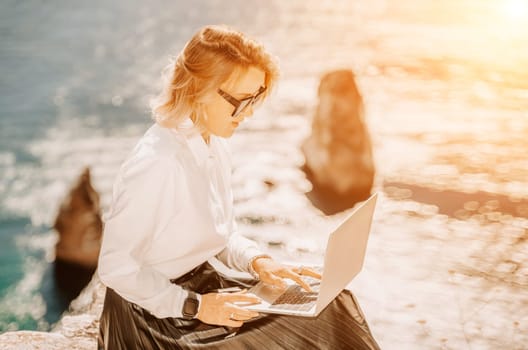 Business woman on nature in white shirt and black skirt. She works with an iPad in the open air with a beautiful view of the sea. The concept of remote work