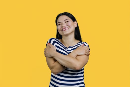 Happy young beautiful woman hugging herself isolated on the yellow background. Self care and self esteem concept.