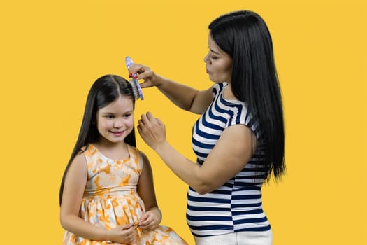 Young asian mother is combing her daughter. Isolated on yellow.