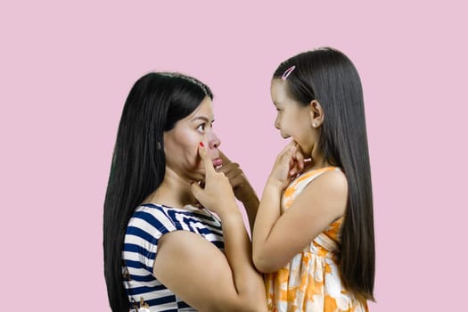 Side view of woman and little girl are making faces to each other. Isolated on pink background.