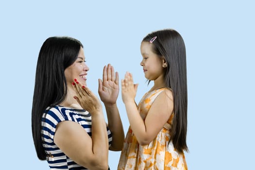 Side view of woman and her daughter are playing clapping game. Isolated on pale blue.