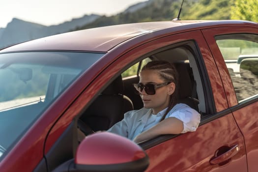 Woman driving a car. A lady in sunglasses takes the wheel of her new car. Rides along the road against the backdrop of mountains and the sea