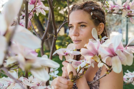 Magnolia flowers. Happy woman enjoys by blooming magnolia tree and sniffs it flowers with closed eyes in spring garden. Portrait