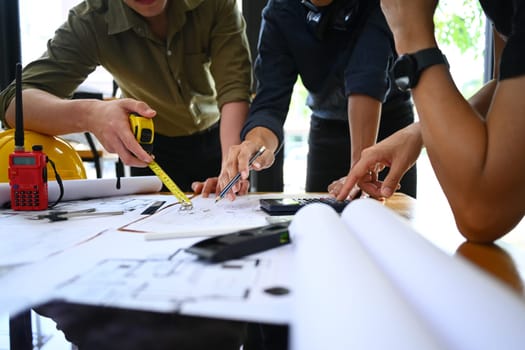 Architect team working with blueprints, planning development details together at meeting table. Cropped shot.