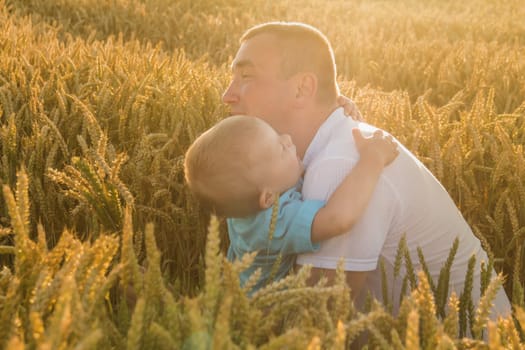 Dad hugs and kisses his little son tightly and merrily walks through the field with ripe wheat. Grain for baking bread. the concept of the love of children and parents and their relationship