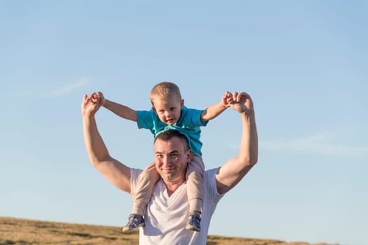 Dad and his little son are having fun walking in a field with ripe wheat. The child is sitting on the shoulders of the father. Grain for making bread. the concept of economic crisis and hunger