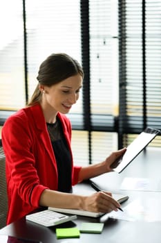 Attractive caucasian businesswoman using digital table and making important notes at working desk.