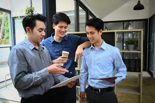 Group of business colleagues discussing project or sharing news during coffee break in office.