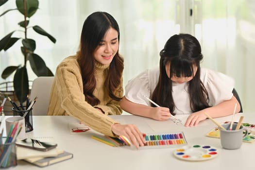 Concentrated little asian girl drawing with her mother in living room. Family home leisure concept.