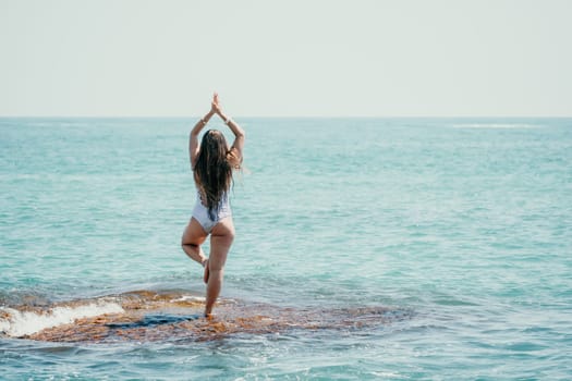 Woman sea yoga. Back view of free calm happy satisfied woman with long hair standing on top rock with yoga position against of sky by the sea. Healthy lifestyle outdoors in nature, fitness concept.