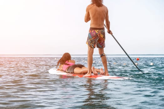 Sea woman and man on sup. Silhouette of happy young woman and man, surfing on SUP board, confident paddling through water surface. Idyllic sunset. Active lifestyle at sea or river