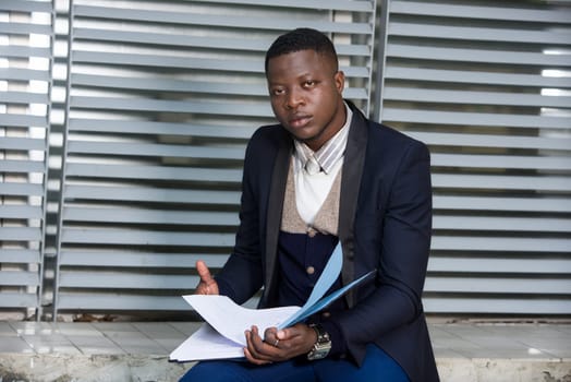 young businessman sitting in a suit looking at the camera with document in hand.