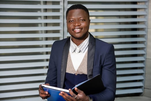 young businessman sitting in suit looking at camera smiling with document in hand.