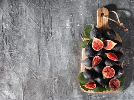Figs with copy space. Top view of whole and half fresh purple figs on wooden cutting board over gray background.