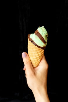 Summer, vacation, ice cream. The hand holds soft ice cream in a chocolate-mint waffle cup. On a black background, close-up