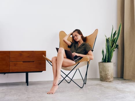 Female student study sits on a chair with a laptop work at home smile and relax, modern stylish interior Scandinavian lifestyle, copy space. High quality photo