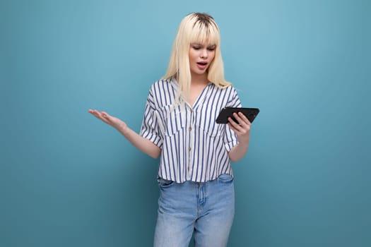 blond young woman in shirt watching video on smartphone on studio background with copy space.