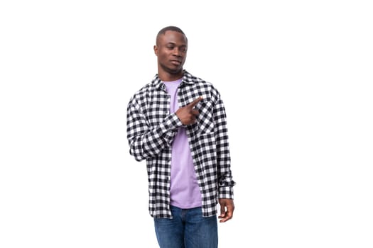 handsome 30 year old african guy dressed in a plaid black and white shirt points with his hand on the background with copy space.