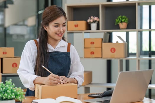 Woman who e-commerce business is writing a list of customers on paper before shipping to them, she runs an e-commerce business on websites and social media. Concept of selling products online.