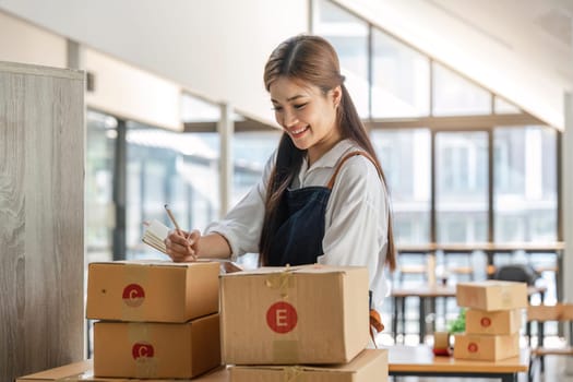 Woman who e-commerce business is writing a list of customers on paper before shipping to them, she runs an e-commerce business on websites and social media. Concept of selling products online.