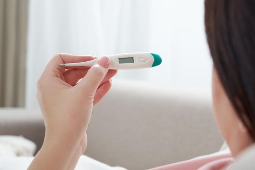 Woman looking at thermometer. Female hands holding a digital thermometer. Girl measures the temperature. Concept of fever, flue or virus