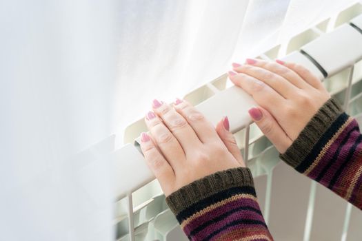 Girl warms up the frozen hands above hot radiator, close up