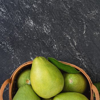 Fresh pomelo, grapefruit in bamboo basket with green leaf on dark black slate background. Seasonal fruit for Mid-Autumn Festival. Top view. Flat lay.