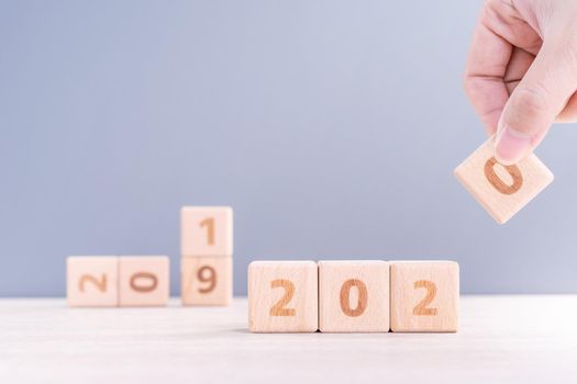 Abstract 2020 & 2019 New year countdown design concept - woman holding wood blocks cubes on wooden table and blue background, close up, copy space.