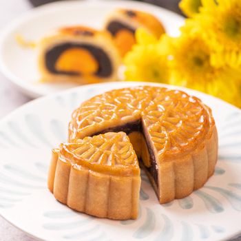 Mid-Autumn Festival traditional food concept - Beautiful cut moon cake on blue pattern plate on white background with flower, close up, copy space