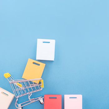 Abstract design element, concept of annual sale, shopping season - mini yellow cart with paper bag isolated on pastel blue background, top view, flat lay.