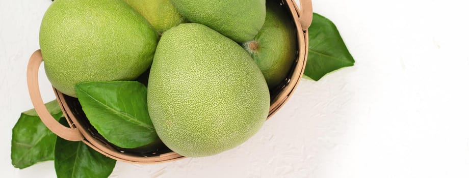 Fresh pomelo, pummelo, grapefruit, shaddock on white cement background in bamboo basket. Autumn seasonal fruit, top view, flat lay, tabletop shot.