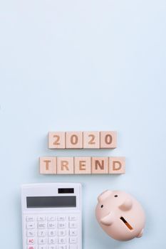 2020 goal, finance plan abstract design concept, wood blocks on blue table background with piggy bank and calculator, top view, flat lay, copy space.