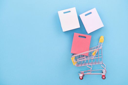 Abstract design element, concept of annual sale, shopping season - mini yellow cart with paper bag isolated on pastel blue background, top view, flat lay.