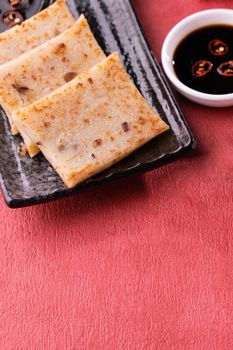 Chinese lunar new year food concept, Delicious turnip radish cake, local cuisine in restaurant with soy sauce on red background, close up, copy space