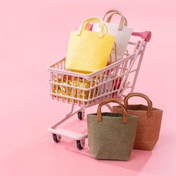 Annual sale shopping season concept - mini red shop cart trolley full of paper bag gift isolated on pale pink background, blank copy space, close up
