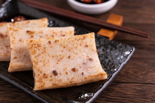 Delicious turnip cake, Chinese traditional local dish radish cake in restaurant with soy sauce and chopsticks, close up, copy space.