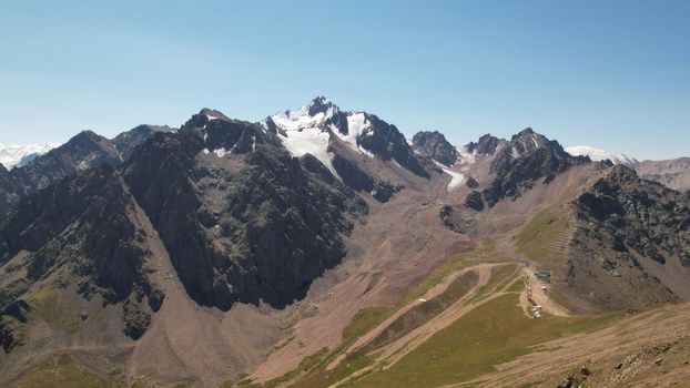 High mountains covered with snow in places. Green grass grows. Huge rocks and cliffs. In the distance, you can see peak of Talgar and Nursultan. A rocky gorge. Rowing peaks from a height. Kazakhstan