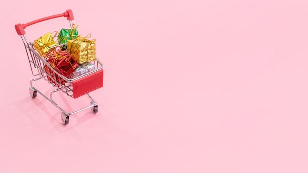 Annual sale, Christmas shopping season concept - mini red shop cart trolley full of gift box isolated on pale pink background, copy space, close up